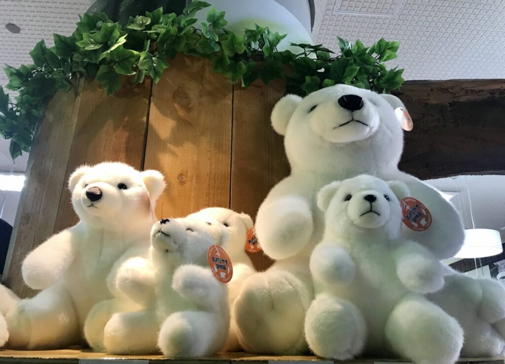 木の棚の上に並べられた白くまのぬいぐるみたち。葉っぱの装飾の下に大小さまざまなサイズのぬいぐるみが並ぶ。