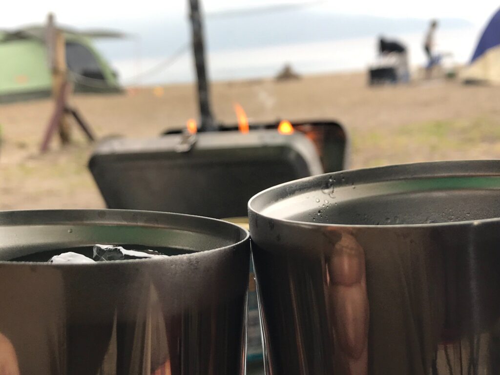 焚き火を前に乾杯するステンレスタンブラー越しの景色