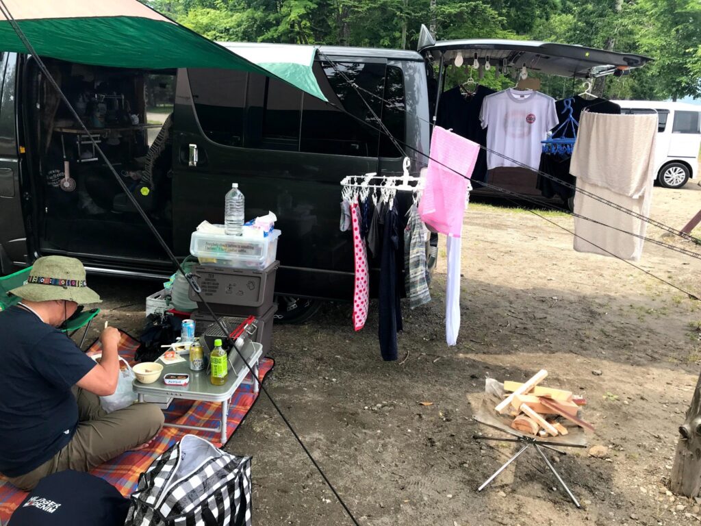 車中泊用ハイエースの横で洗濯物を干しながら食事する様子