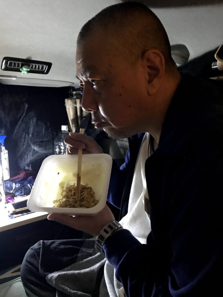車中泊中の車内で、焼きそばを真剣に食べる男性のアップ