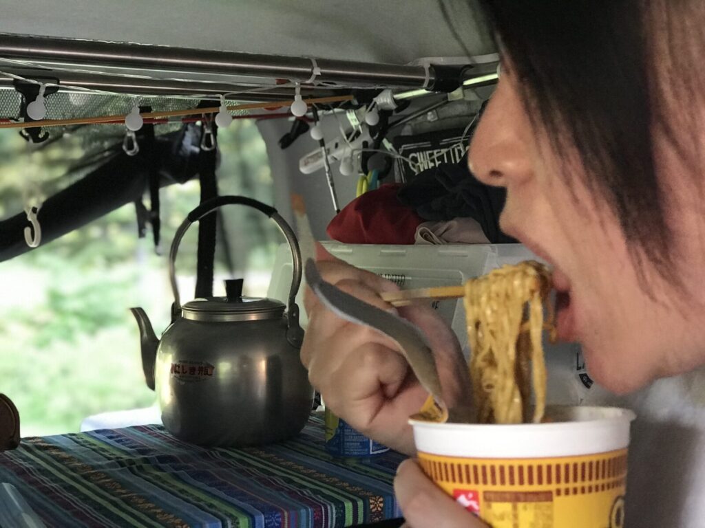 キャンピングカーの中で、カップラーメンを勢いよくすする女性の横顔