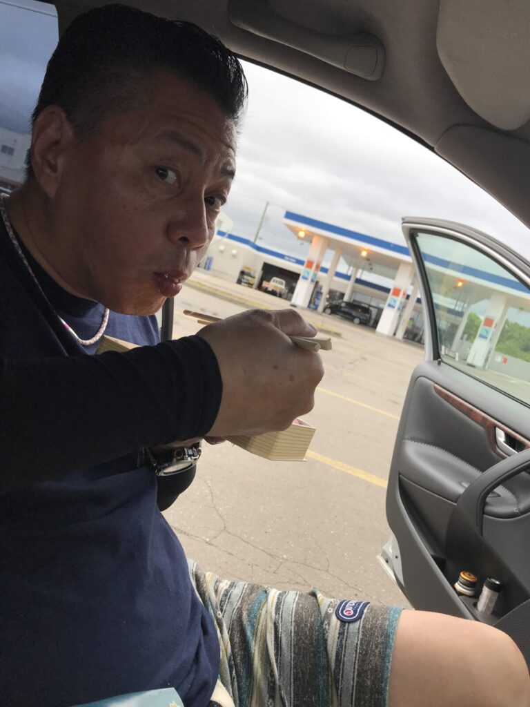 車の助手席で駅弁を食べている男性。かにめしを楽しんでいる表情が印象的