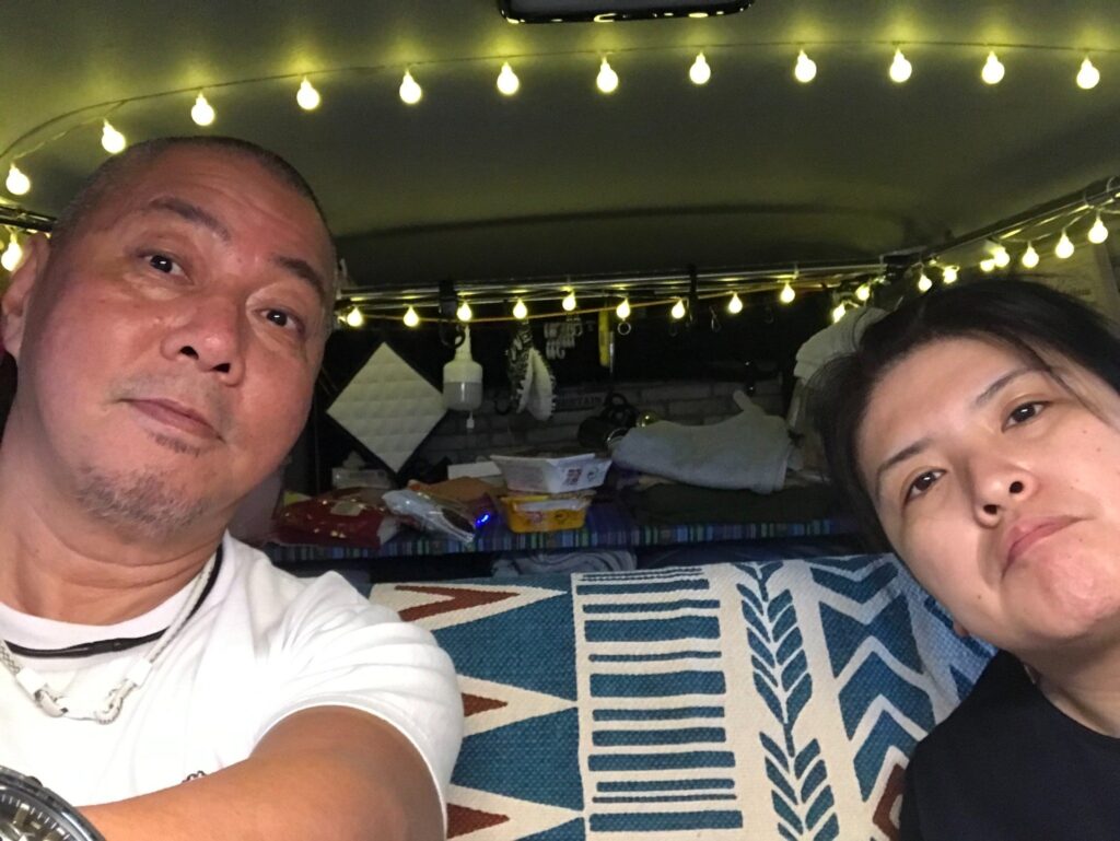 ハイエースの車内でくつろぐ夫婦の様子(夜・ライト付き)