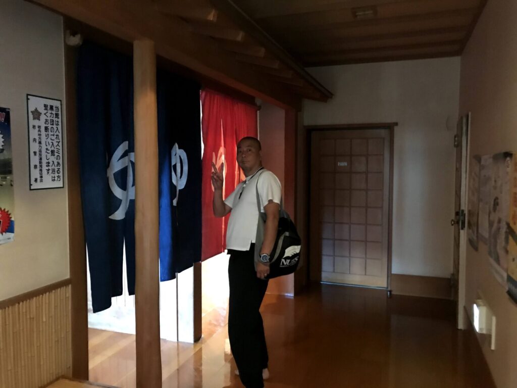 のれん前でピースする男性と温泉入口の様子