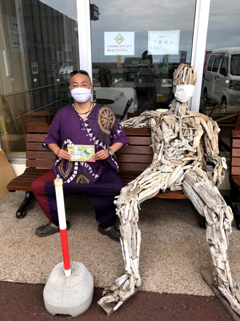道の駅で流木人形と一緒に記念撮影をする男性の様子