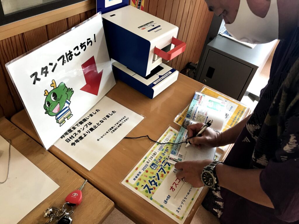 スタンプラリー帳に日付を記入している様子と、道の駅のスタンプ台が設置された様子