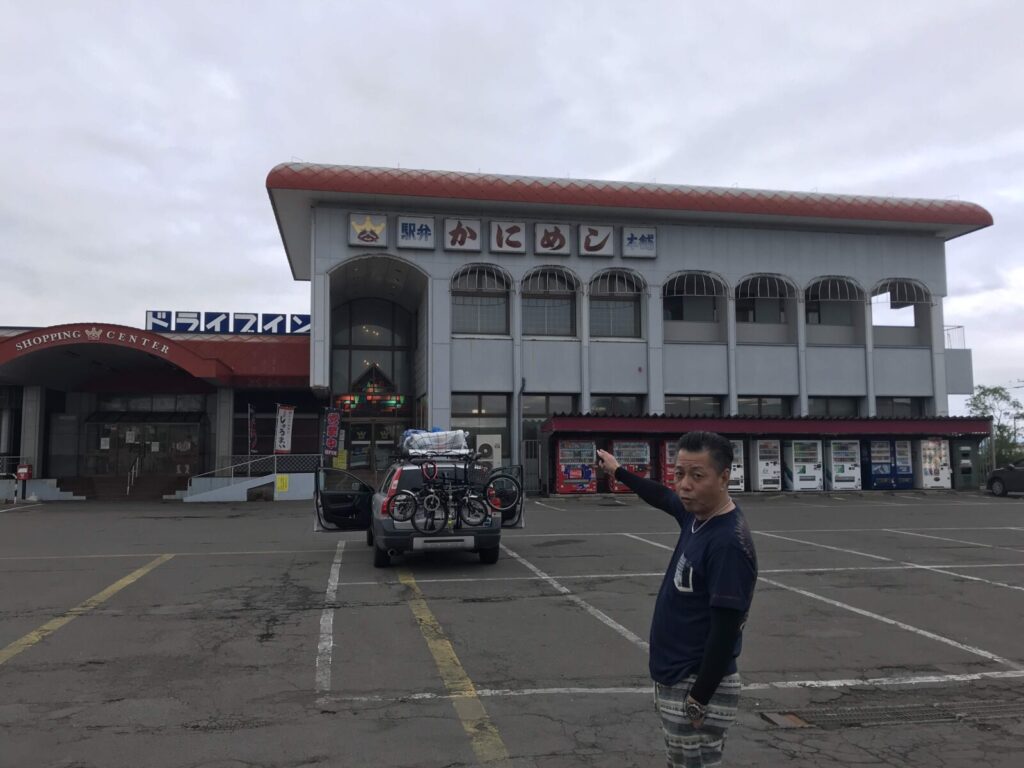 駅弁「かなやのかにめし」の本店外観。レトロな雰囲気のドライブインと男性の指さしポーズ