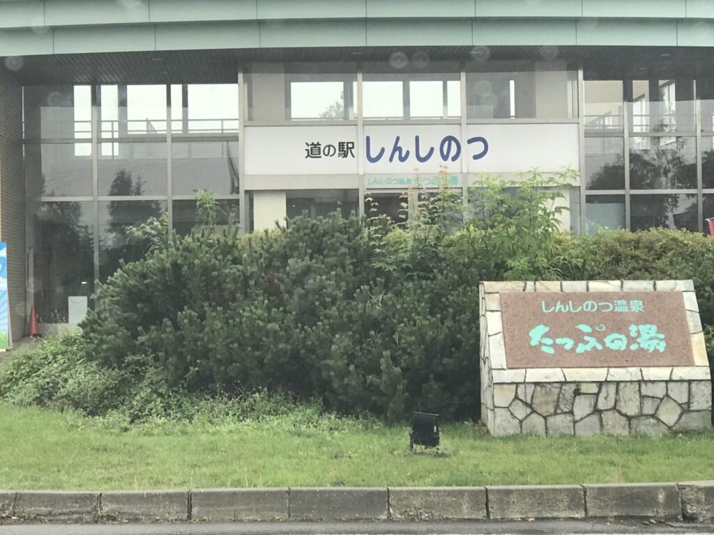 「たっぷの湯」と書かれた温泉の看板と入口周辺の植え込み