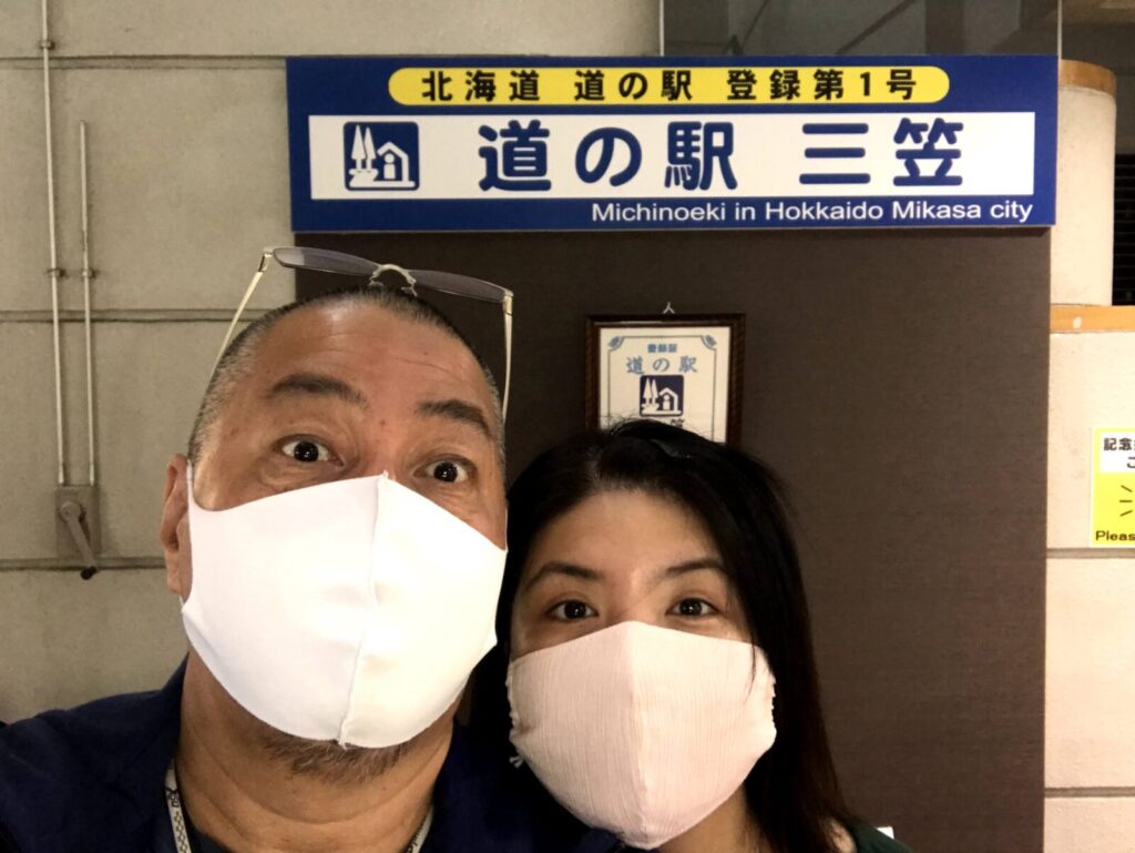 道の駅三笠の看板前で記念撮影する2人