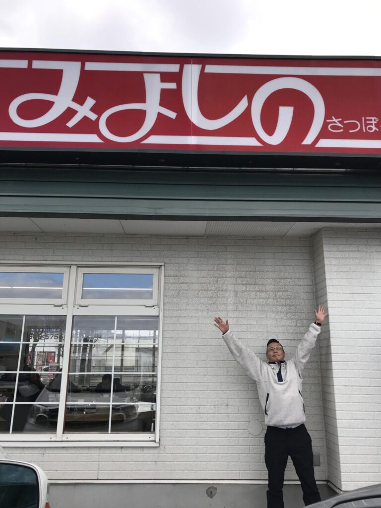 2017年、みよしの店舗前で看板に向かって両手を上げる男性の様子