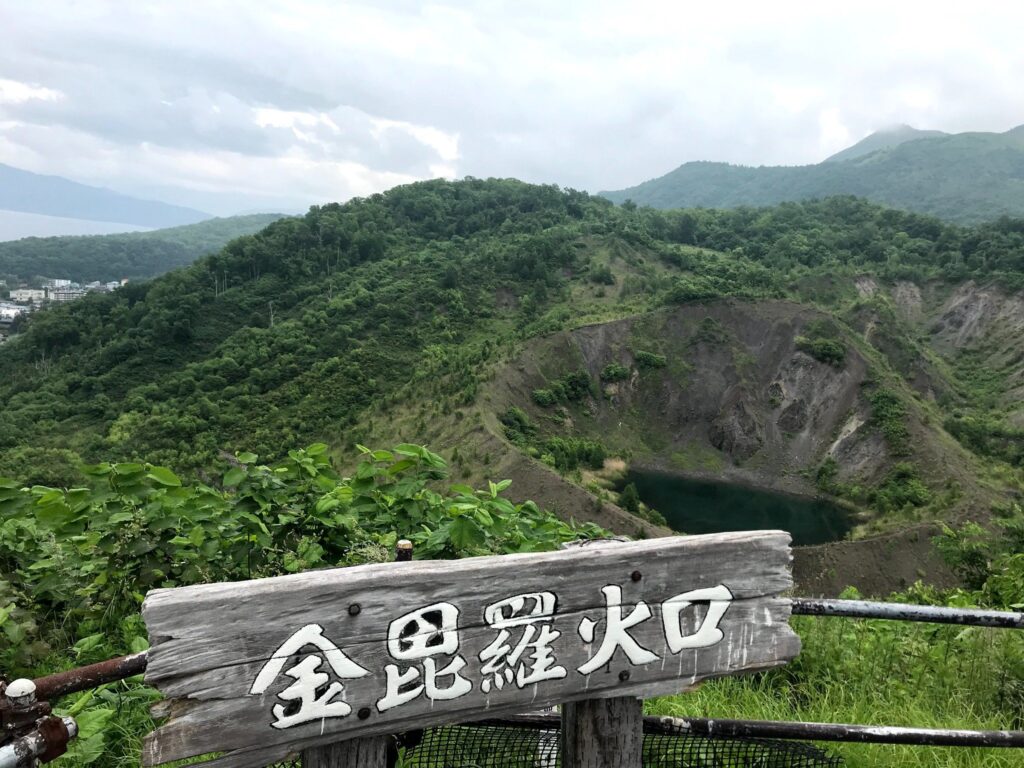 緑に囲まれた金毘羅火口とその案内看板
