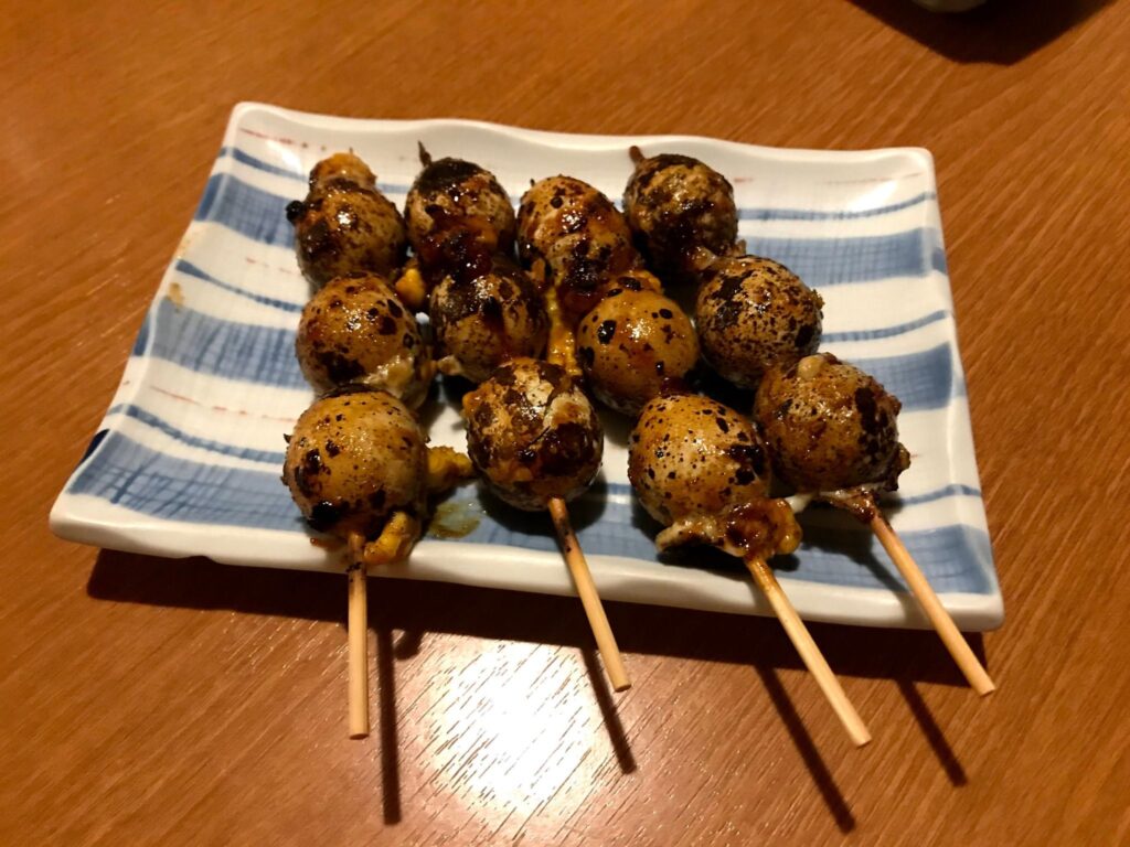 白い角皿に並べられた、焼き色のついたうずらの卵串料理