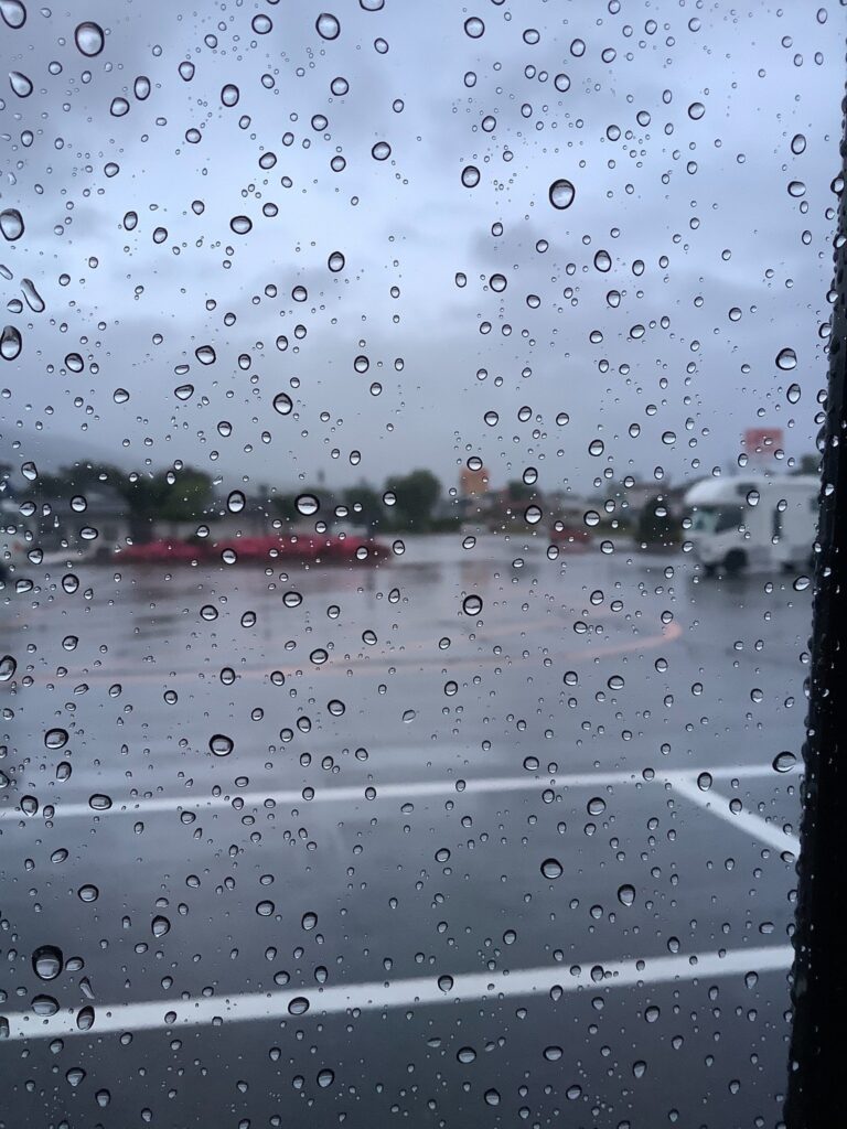 雨が降る駐車場を車内から見た風景。窓には無数の水滴が付いている。