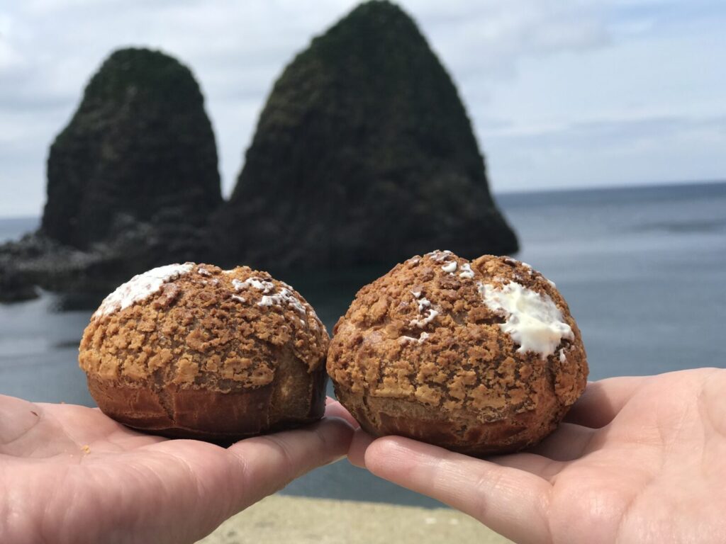 手のひらに乗った2つの岩シューと背景の三本杉岩