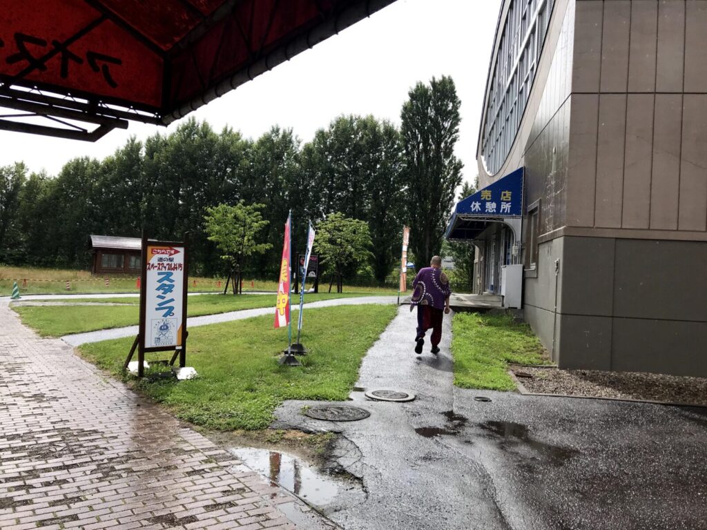 雨の中、スペース・アップルよいちに向かう男性の後ろ姿