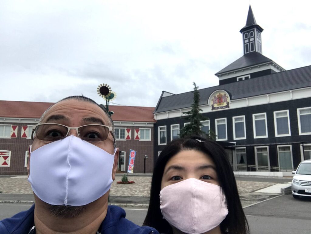 マスク姿の男女が「道の駅サンフラワー北竜」の建物前で自撮りしている様子