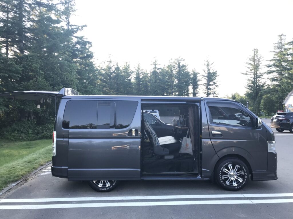 駐車場に停められたキャンピング仕様のハイエースの横からの写真