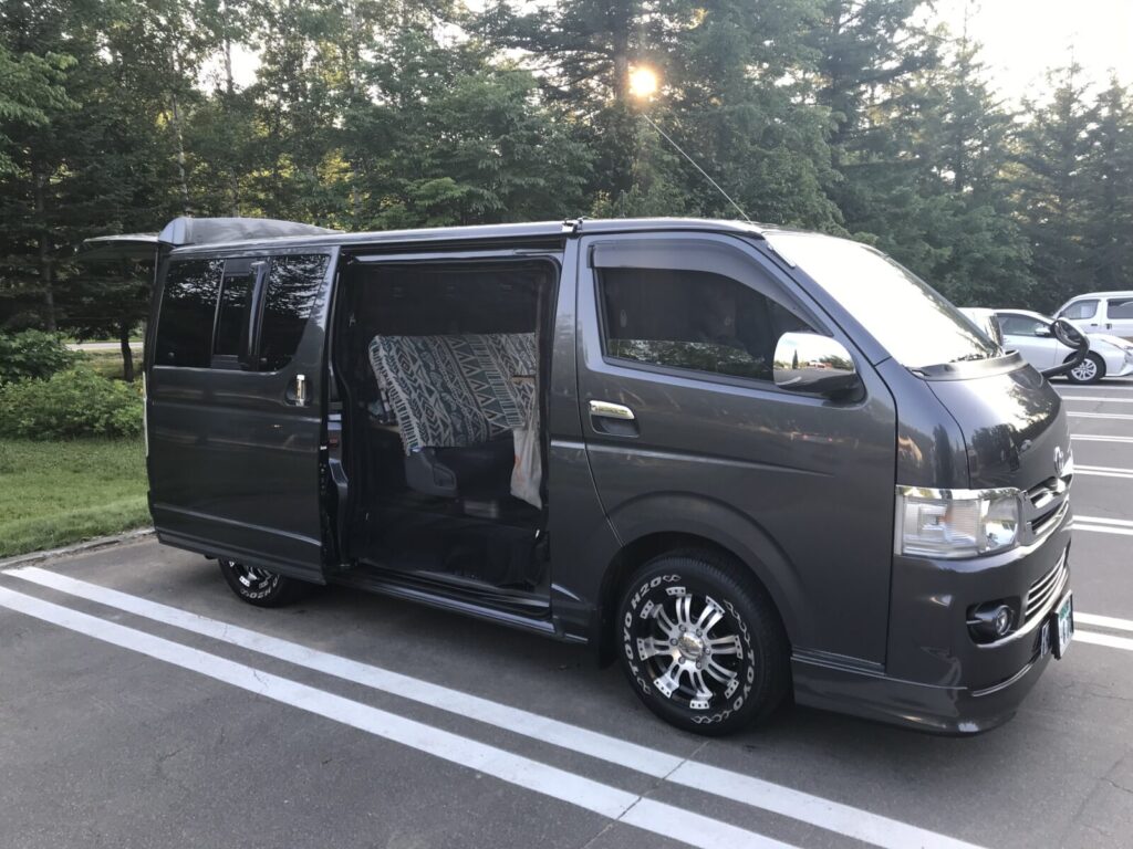 車中泊仕様のハイエースを駐車場で撮影、外観と開いたスライドドアが写る