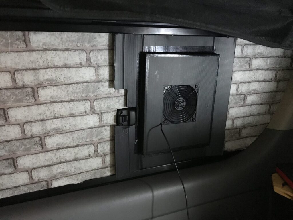 車中泊車の窓に取り付けられたファン付き換気パネルの写真