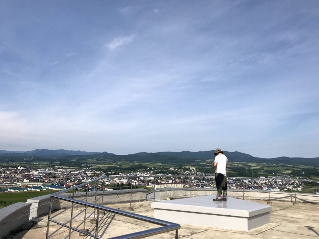 展望台に立つ男性が、広がる上富良野の市街地と山々の風景を眺めている様子