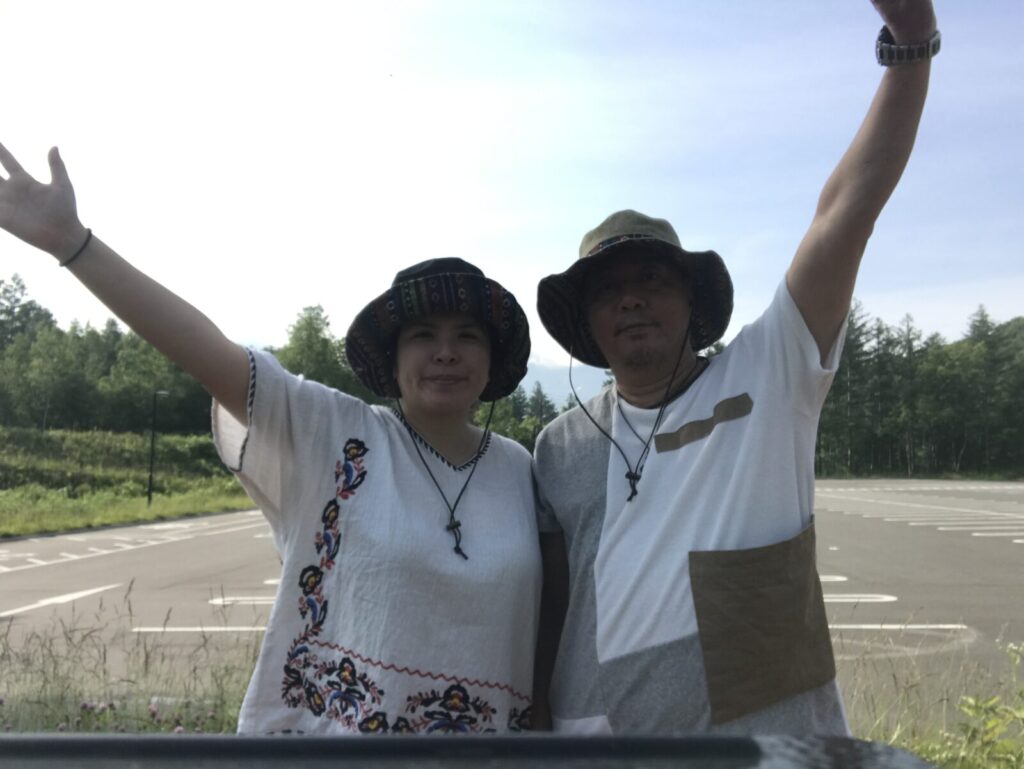 帽子をかぶった男女が駐車場で両手を上げてポーズをとっている様子