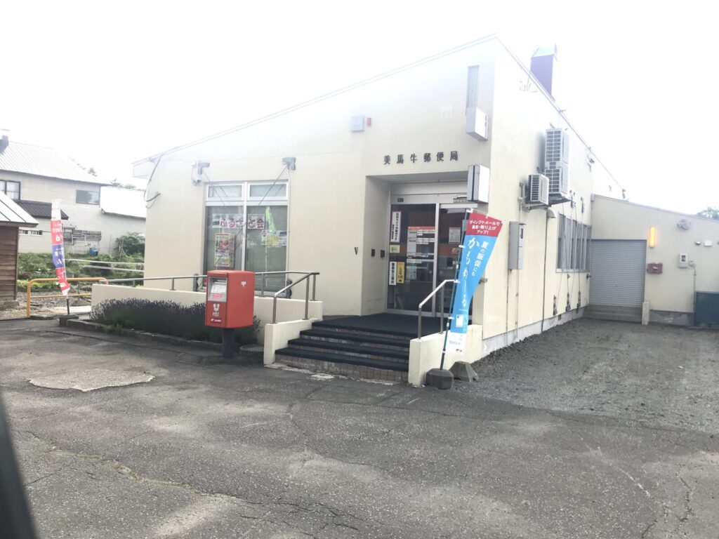 美馬牛郵便局の外観。赤いポストと青いのぼりが立つ建物。