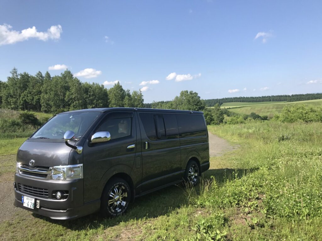 美瑛の丘の空き地に停車したハイエースと、周囲に広がる緑の風景。