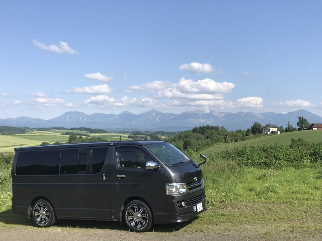 美瑛の丘に停車したハイエースと、遠くに広がる大雪山の稜線。