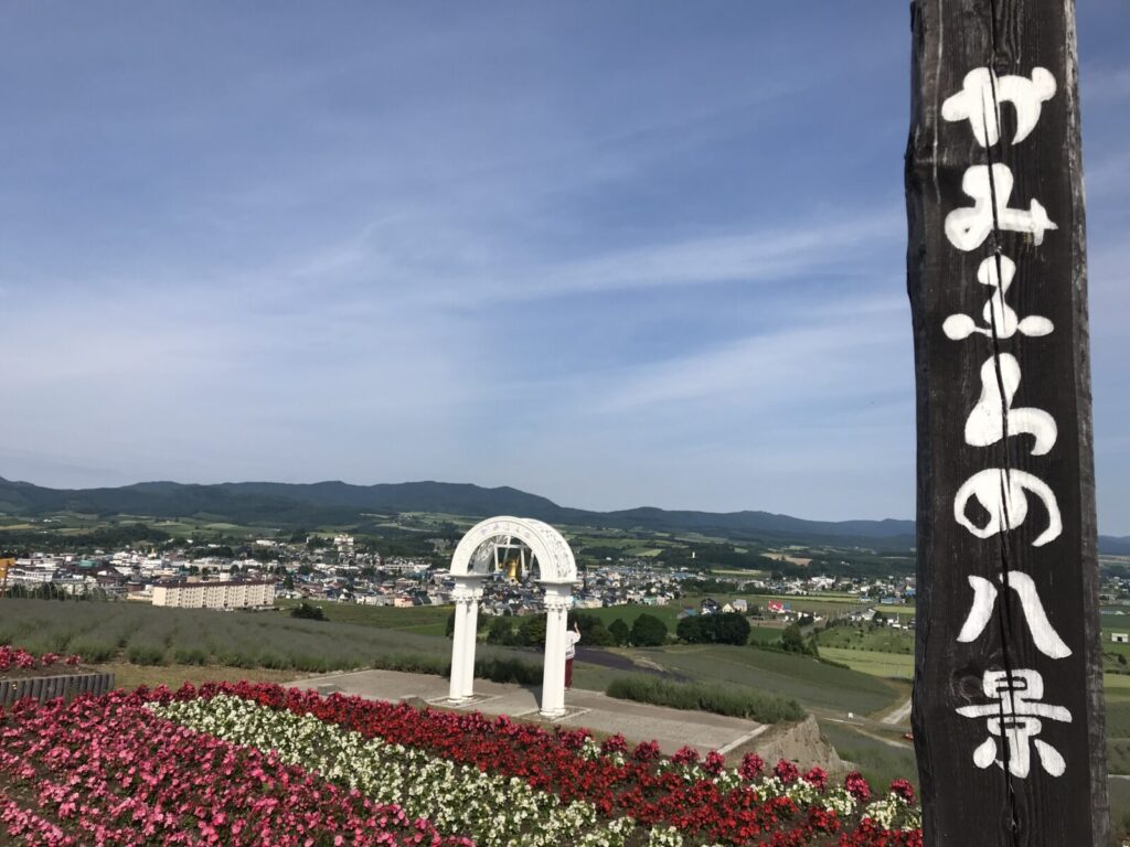 「かみふらの八景」と書かれた柱と、色とりどりの花と白いアーチの鐘