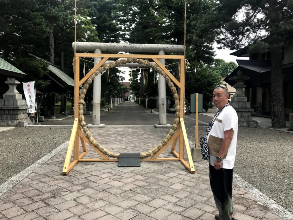 富良野神社の茅の輪くぐりの前に立つ男性と鳥居、初夏の境内の風景