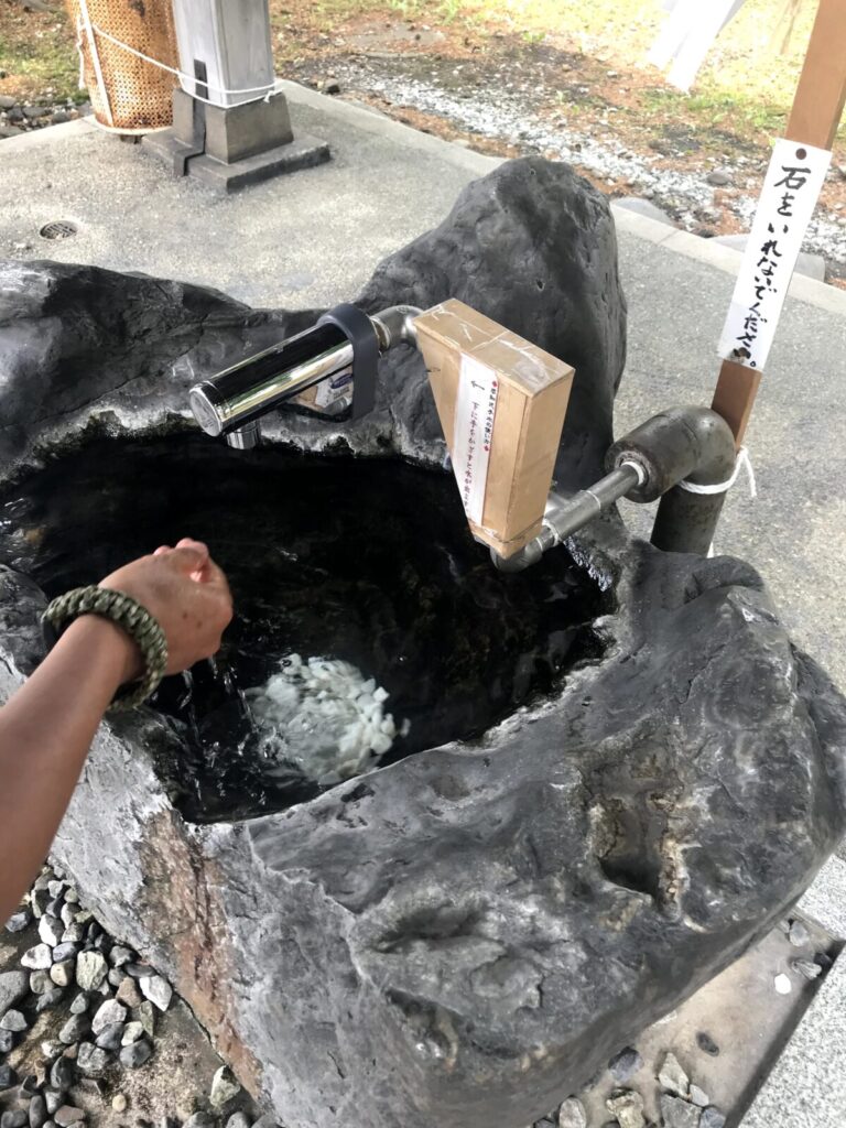 富良野神社の手水舎で手を清める様子、石の水槽と自動水栓が印象的