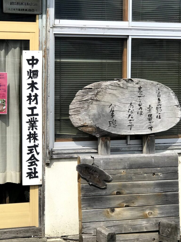 中畑木材工業の入り口横に置かれた木製の看板と詩が刻まれた木の板。年月を感じさせる風合い。