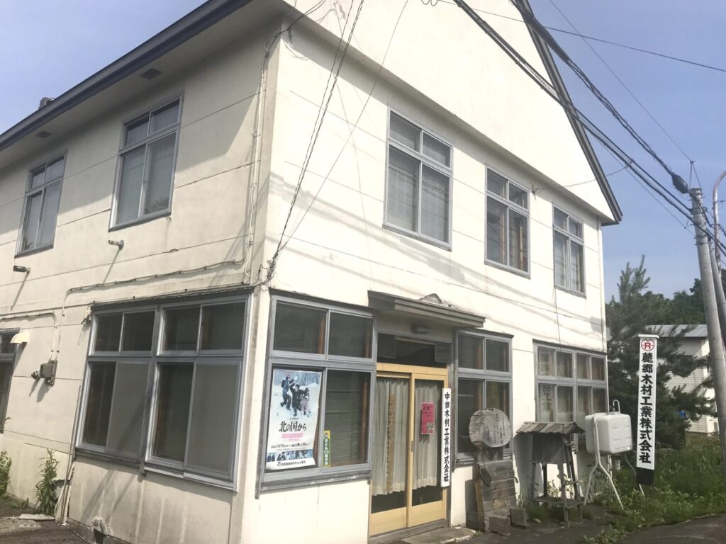 「中畑木材工業株式会社」の建物全体と正面入り口の様子。昔ながらの雰囲気が残る白い建物が印象的。