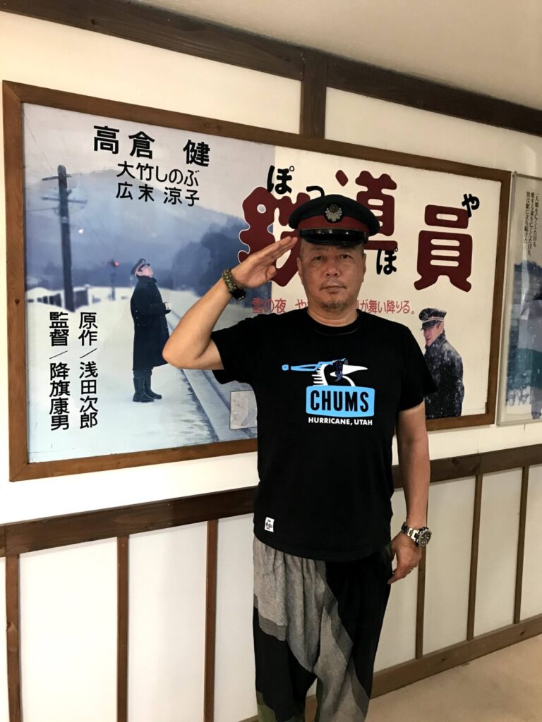 『鉄道員』のポスター前で駅員帽をかぶって敬礼する男性