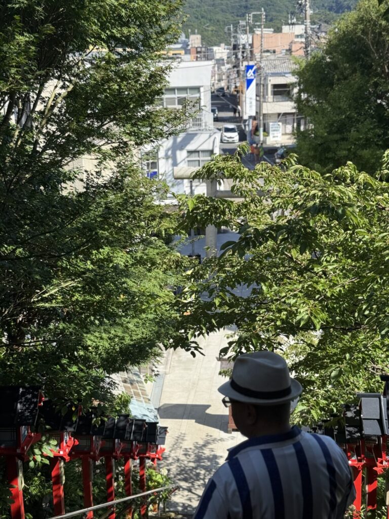 神社の石段上から市街地を見下ろす景色と男性の後ろ姿