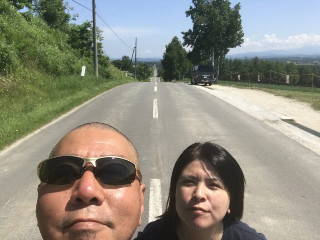 一直線の道を背景にした夫婦の自撮り写真(上富良野)