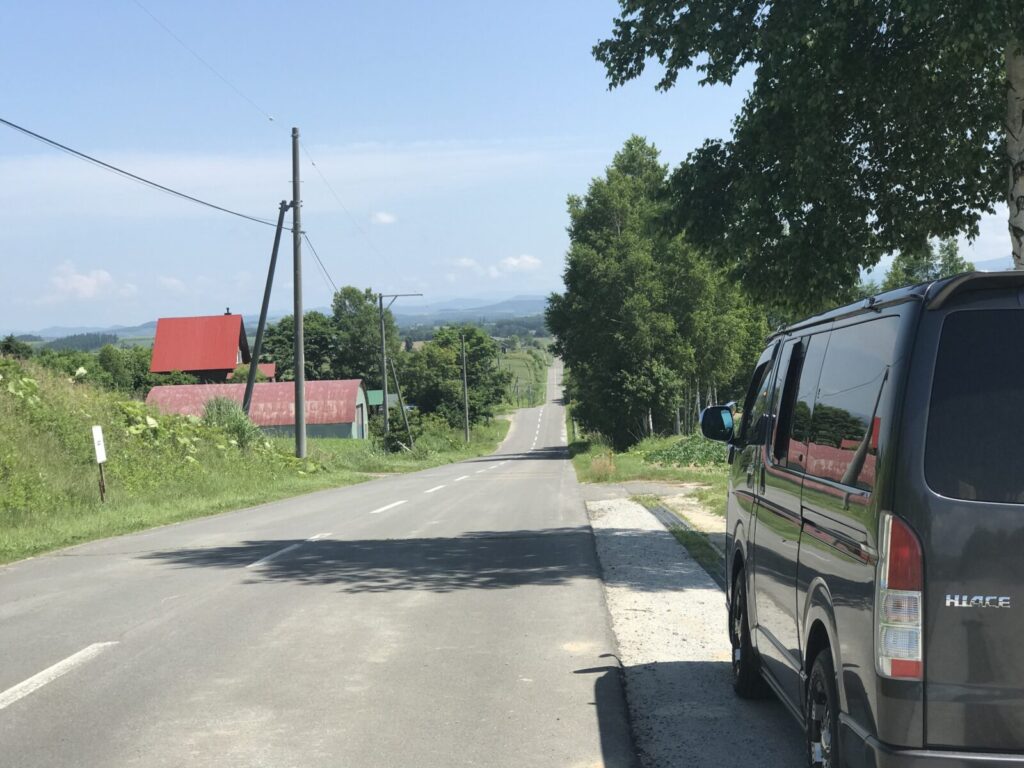 ジェットコースターの路の駐車スペースに停めたバンと一直線に続く道の風景(上富良野)