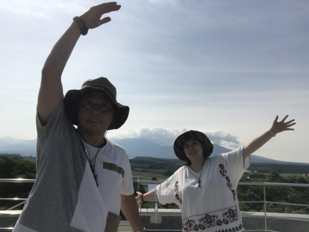 上川の展望台で元気ポーズをする夫婦と背景の山々