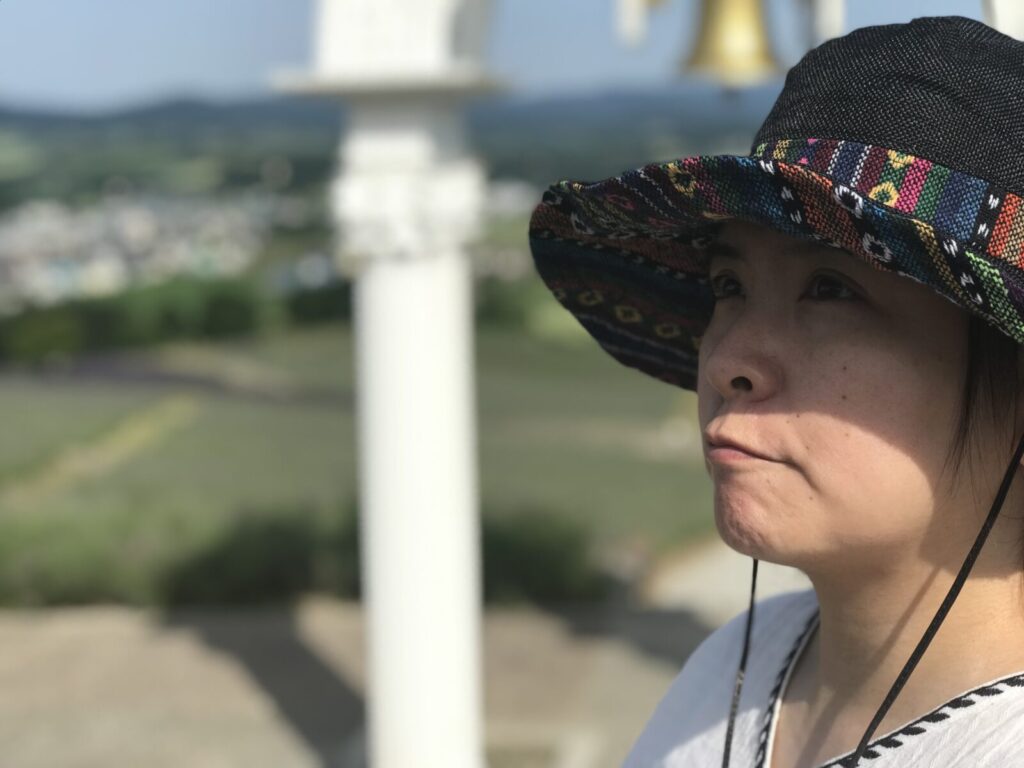 幸せの鐘を見上げるくま嫁の横顔とラベンダー畑