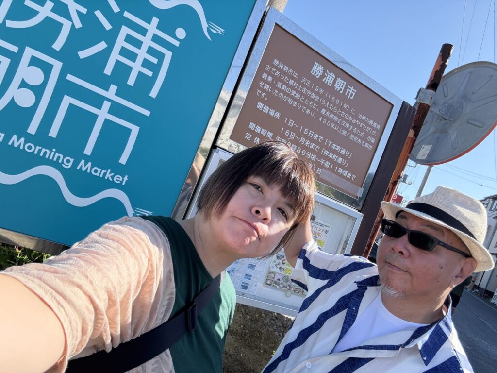 勝浦朝市の看板前で記念撮影する夫婦