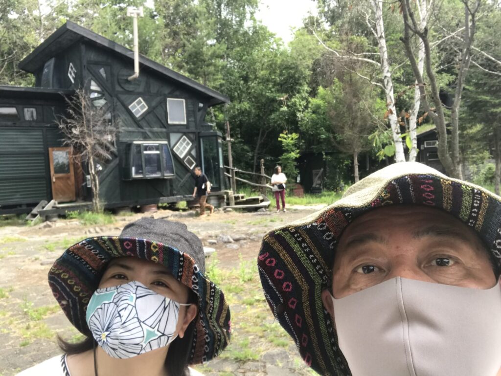拾って来た家の前で観光中の人々と一緒に写る夫婦の記念写真