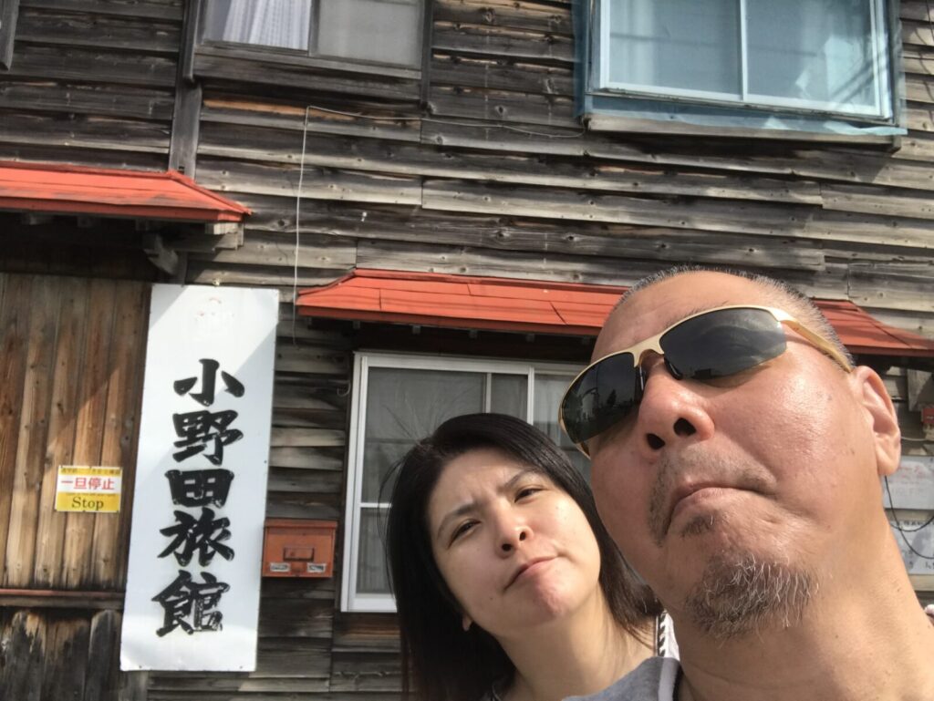 木造の小野田旅館を背景に、夫婦で並んで撮影したセルフィー