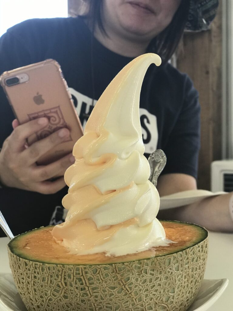 メロンにのったミックス味のソフトクリームと女性