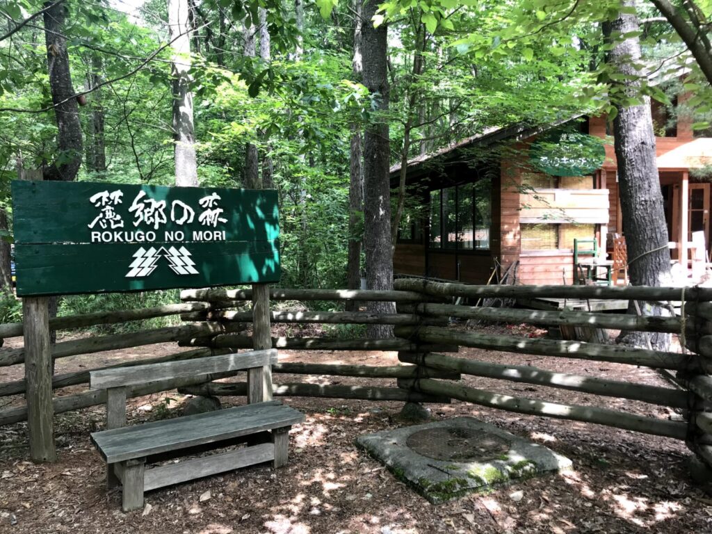 「北の国から」の舞台、麓郷の森の入口。緑の中に木製の看板とベンチが設置されている。