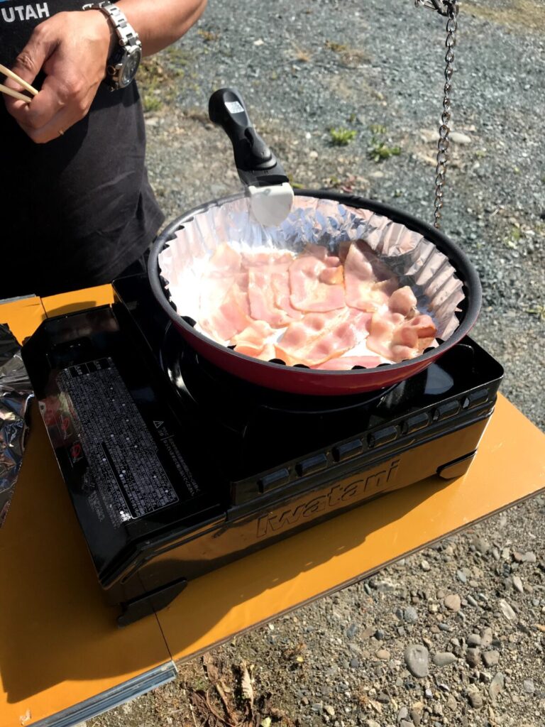 車中泊の朝ごはんとしてカセットコンロでベーコンを焼いている様子