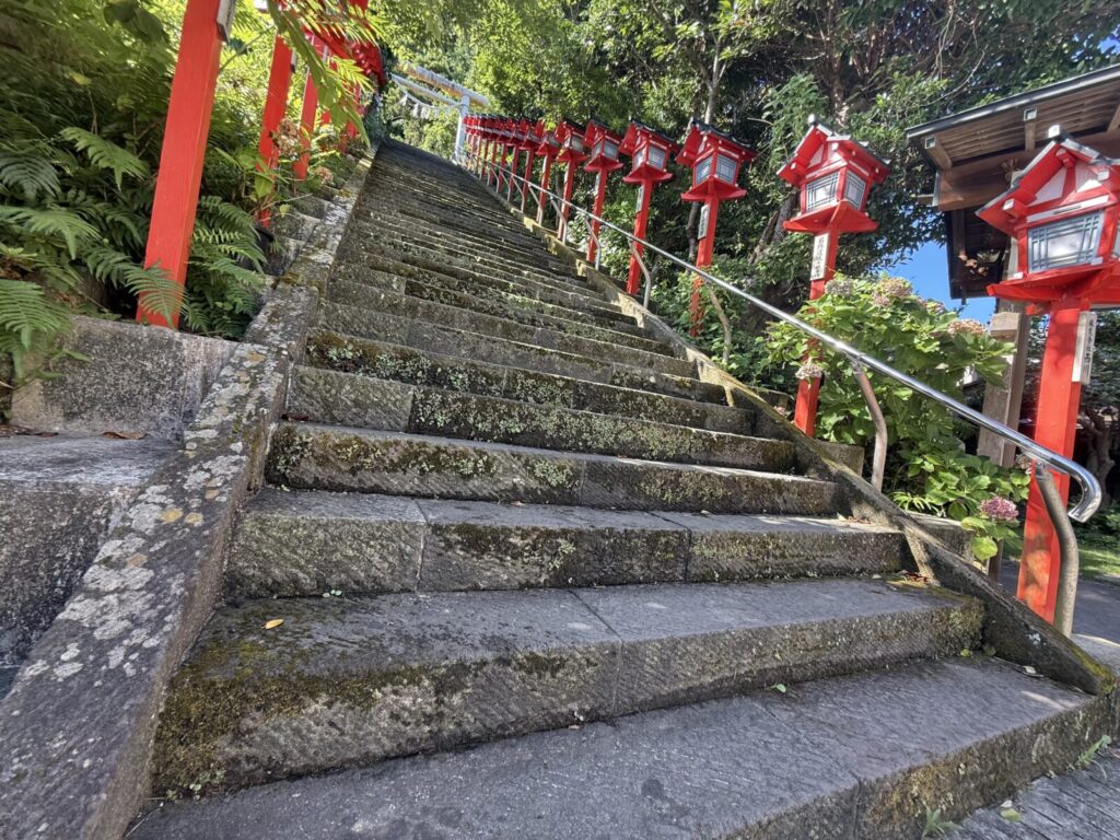 赤い灯篭が並ぶ苔むした石段が続く遠見岬神社の参道