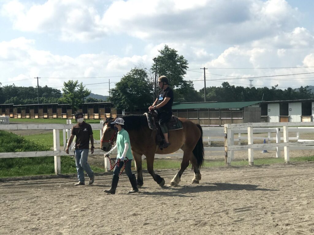 馬に乗って親指を立てる男性と付き添うスタッフ(うりまく乗馬体験)