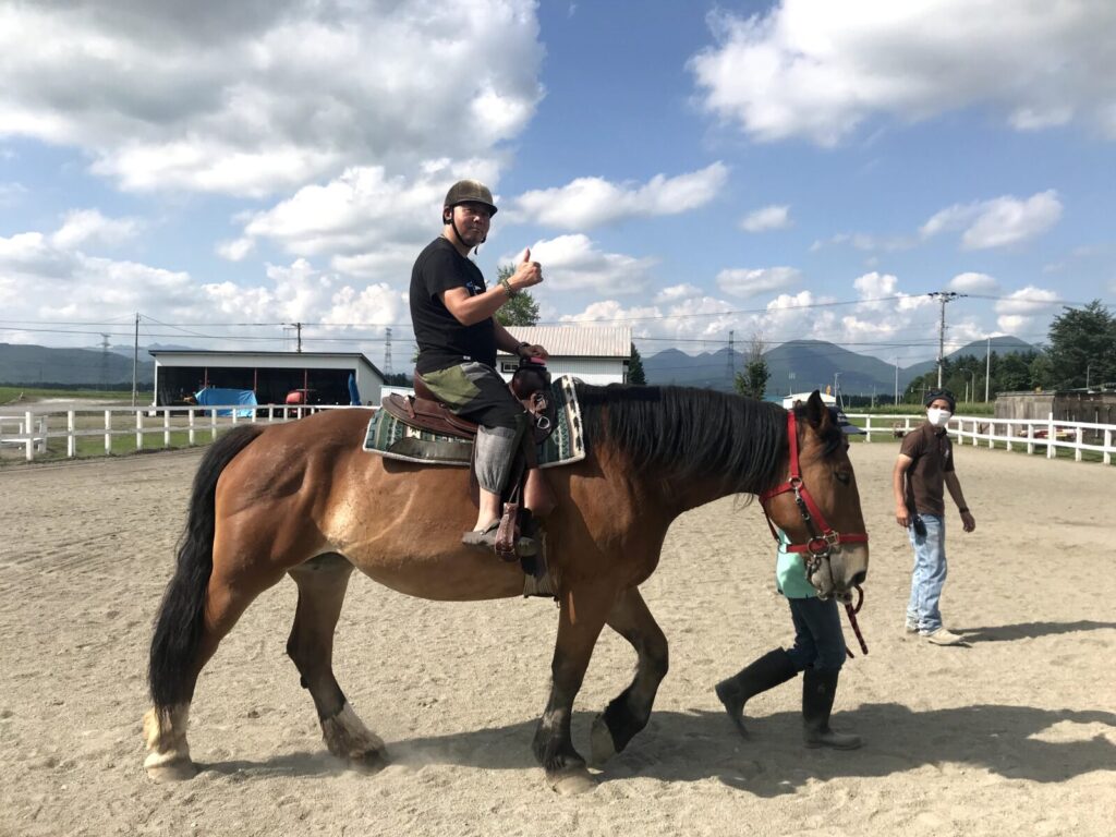 馬に乗って親指を立てる男性と付き添うスタッフ(うりまく乗馬体験)