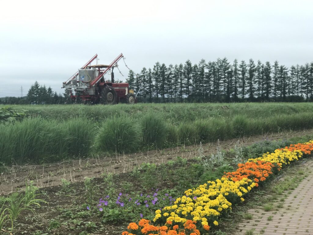 農地と色鮮やかな花壇、後方に大型トラクターが見える風景