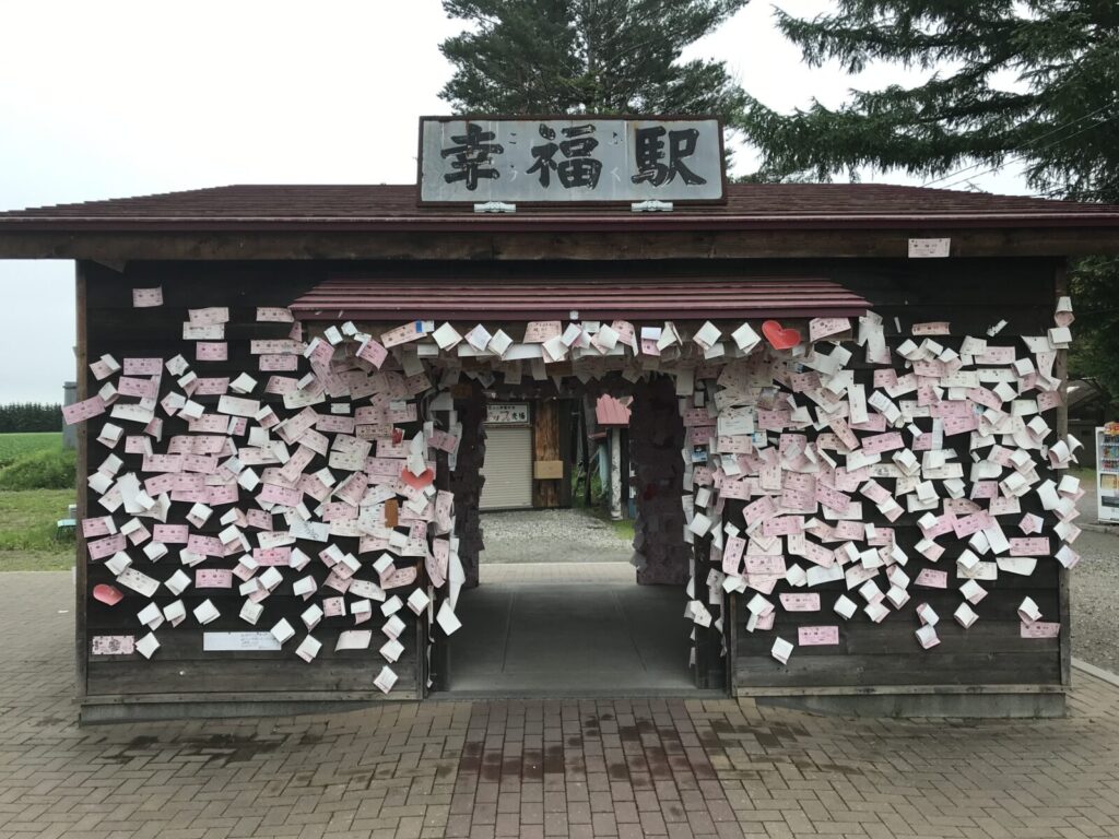 幸福駅の外観と無数のピンクの切符が貼られた小屋
